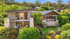 A modern two-story house with a balcony, a patio with outdoor furniture, and a well-maintained garden. - Cohala—Luxe Hillside Retreat with Theatre & Garden (Yallingup)
