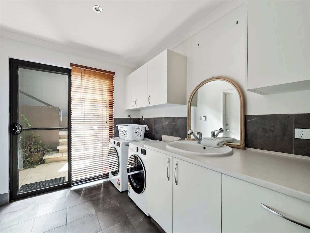 A modern kitchen with a built-in washing machine, a sink, and a large mirror.