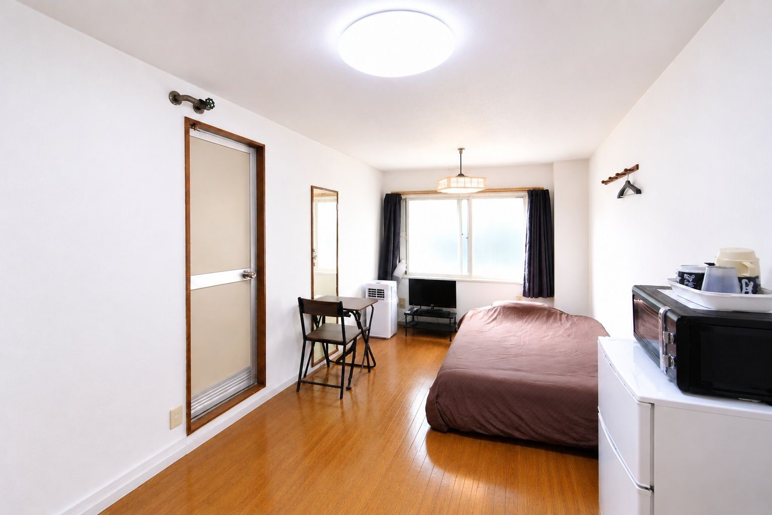 A compact room with a bed, a desk, a chair, a television, and a window with curtains.