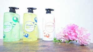 Three bottles of liquid soap on a wooden surface with a pink flower beside them. - Nissho House 105 (Sapporo)