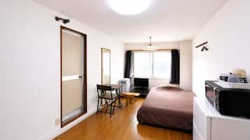 A compact hotel room with a bed, a desk, a chair, a television, and a window with curtains.