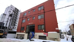 A red building with multiple windows and a sign in Japanese. - Nissho House 105 (Sapporo)