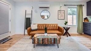 A modern living room with a brown leather sofa, a round mirror, and a coffee table with a colorful abstract design.