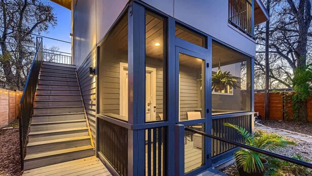 A modern house with a wooden deck, a glass-enclosed porch, and a staircase leading to the entrance.