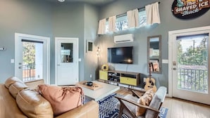 A living room with a beige sofa, a coffee table, a TV, and a guitar. There are two doors, one leading outside and another to a balcony. - Holly Studio walkable to Downtown, bars, SXSW (Austin)