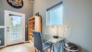 A room with a glass table, a black office chair, a wooden bookshelf, a trash can, and a window with blinds. - Holly Studio walkable to Downtown, bars, SXSW (Austin)