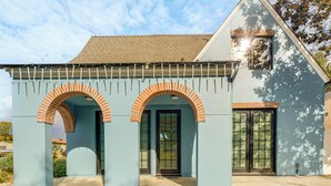 Een modern huis met een lichtblauwe gevel, een entree met een bakstenen boog en een groot raam.
