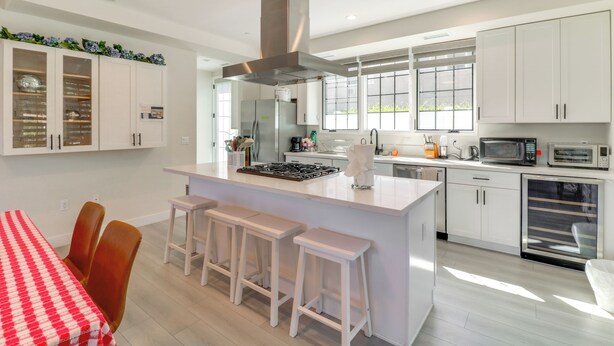 Een moderne keuken met witte kasten, een centraal eiland met krukken, en een eethoek met een rood-wit geruit tafelkleed.