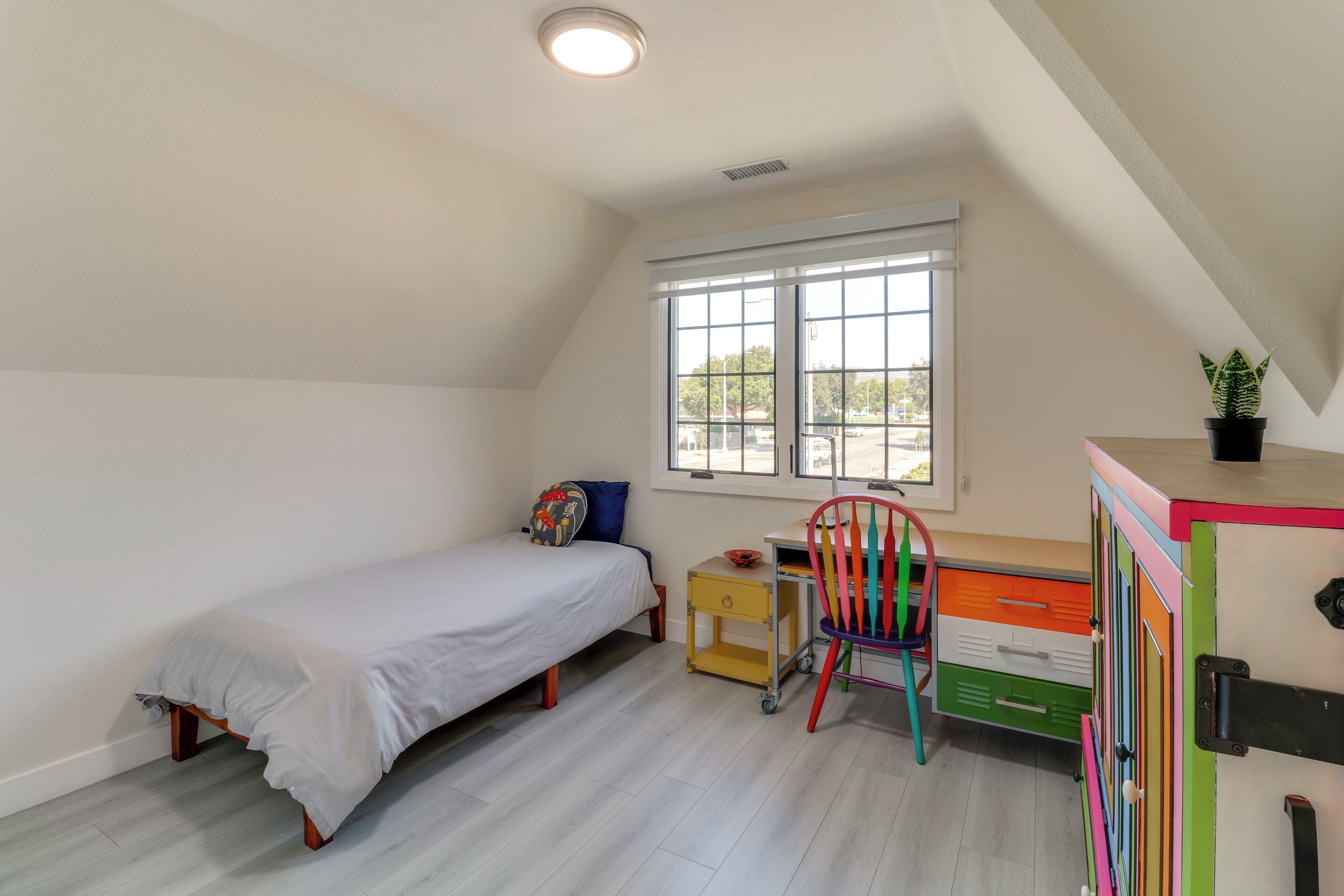 Un dormitorio con una cama individual, un escritorio con silla, una ventana y un mueble de almacenamiento colorido.