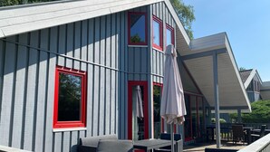 A covered outdoor seating area with a table and chairs, a pergola, and a view of a building with red-framed windows. - Exklusives Skandinavisches Ferienhaus (Mirow)