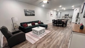 A modern living room with a sofa, coffee table, and a dining area with chairs and a table. - The Gathering Lovely Spacious 5-bedroom House  (Magnolia)