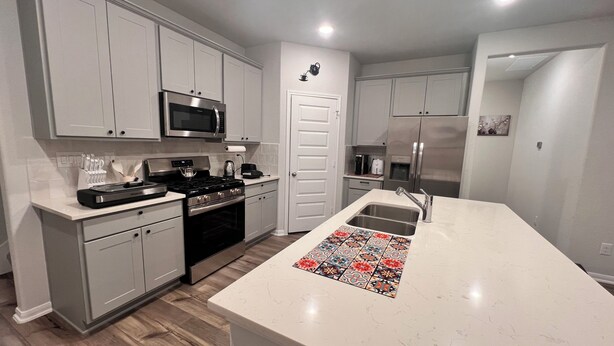 A modern kitchen with white cabinets, stainless steel appliances, and a patterned backsplash. - The Gathering Lovely Spacious 5-bedroom House  (Magnolia)