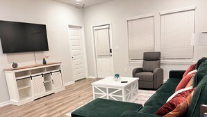 A modern living room with a green sofa, a grey armchair, a white coffee table, and a TV mounted on the wall. - The Gathering Lovely Spacious 5-bedroom House  (Magnolia)