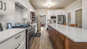 A modern kitchen with white cabinets, stainless steel appliances, and a wooden countertop. - Dino's Last Post | Sleeps 8 | Private Backyard! | (Drumheller)