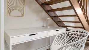 A white desk with drawers, a white chair with a lattice backrest, and a wooden staircase with a decorative railing. - Dino's Last Post | Sleeps 8 | Private Backyard! | (Drumheller)