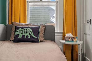 Cozy retreat with a neatly made bed and a bedside table, featuring a unique pillow and a window with curtains.