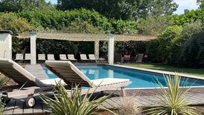 Un área de piscina con sillones de descanso y una pérgola.