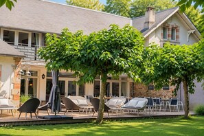 A house with a patio area featuring outdoor seating and a tree providing shade. - Luxurious residence for 30 people, with a pool and a large garden (Garrevaques)