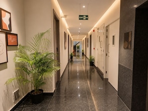 A hotel corridor with framed artwork, potted plants, and an exit sign.