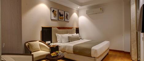 A hotel room with a bed, a chair, a small table with fruit, and artwork on the wall.