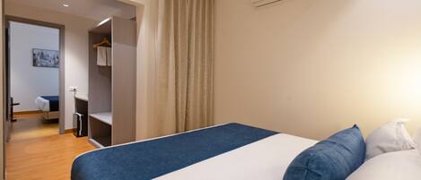 A hotel room with a bed, a wardrobe, a mirror, and a door leading to another room.