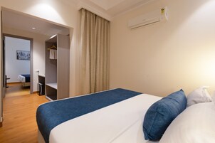 A hotel room with a bed, a wardrobe, a mirror, and a door leading to another room.