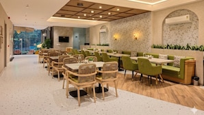 A modern restaurant with a long counter, green upholstered seating, and a patterned wall.