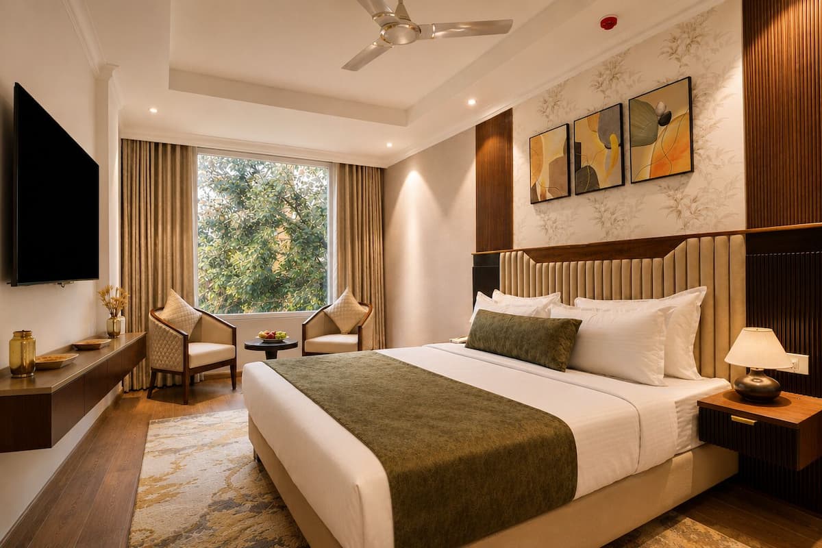 Quarto de hotel com cama, escrivaninha, cadeira, televisão, ventoinha no teto e obras de arte na parede.