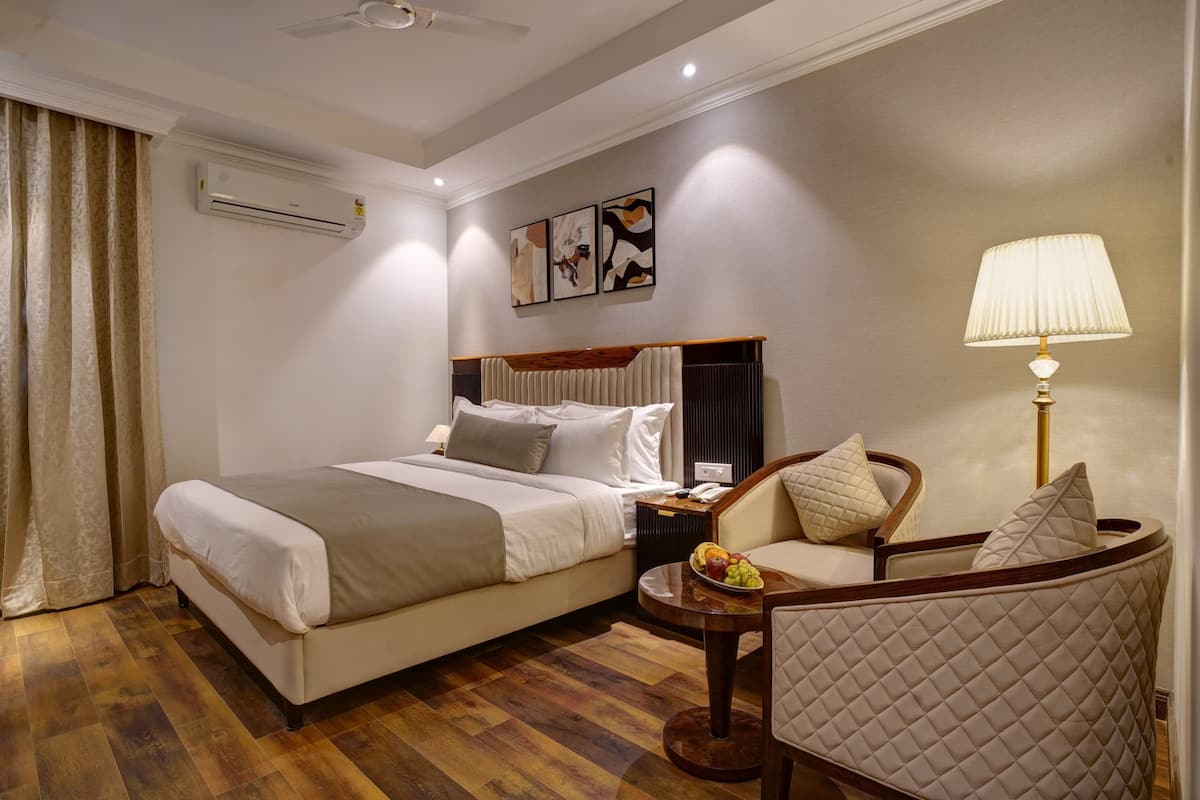 Quarto de hotel com cama, poltrona, mesinha com frutas, ar condicionado e obras de arte na parede.