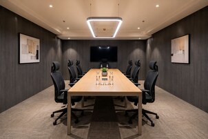 Een vergaderruimte met een lange tafel, zwarte stoelen, een flatscreen televisie en ingelijste kunstwerken aan de wanden.