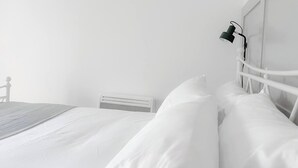 A minimalist bedroom with a white bed, a headboard with a mounted lamp, and a white radiator. - Entire 2 Bedroom House 7m To Station (Barnet)