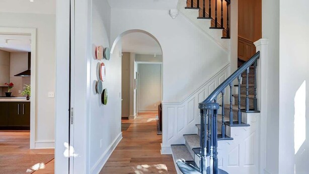Un escalier avec une rampe bleue, un mur blanc avec une porte et un couloir menant à la cuisine.