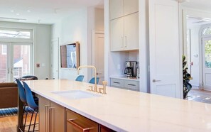 A modern kitchen with a large island, bar stools, and a coffee machine.