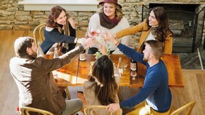 Un groupe de personnes trinquant autour d’une table en bois dans une pièce aux murs de pierre, où se trouve une cheminée.