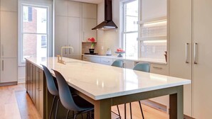 Une cuisine moderne dotée d’un îlot central, de meubles de couleur claire et d’une grande fenêtre qui laisse entrer la lumière naturelle.