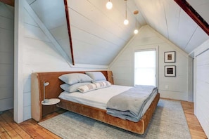 A bedroom with a sloped ceiling, a bed with a wooden headboard, a bedside table, and a window.