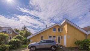 En gul byggnad med en parkerad bil framför, omgiven av grönska.