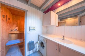 Ein kleines Badezimmer mit einer Holztür zur Sauna, einer Waschmaschine und einem Waschbecken.
