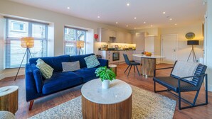 A modern living room with a blue sofa, a round coffee table, and a dining area with a small table and chairs.