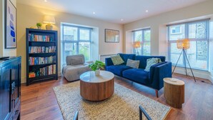 A spacious living room with a blue sofa, a round coffee table, and a bookshelf.