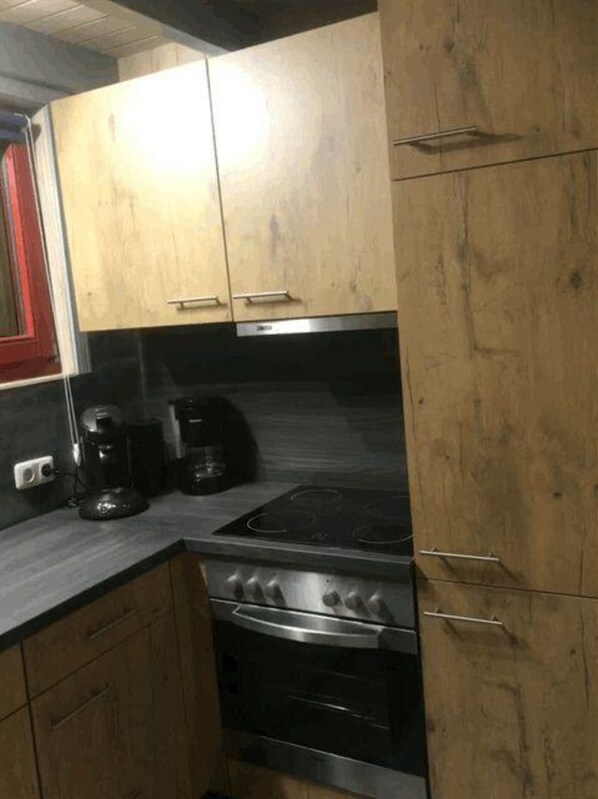 A compact kitchen with wooden cabinets, a gas stove, and a coffee maker. - Exklusives Skandinavisches Ferienhaus (Mirow)