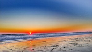 A beach with a sunset, waves, and a clear sky.