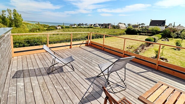 A wooden deck with two folding chairs and a table, overlooking a grassy area and houses.
