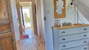 A spacious room with a wooden floor, a white dresser, a chandelier, and a large mirror.