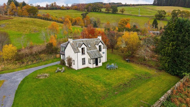 Une maison blanche avec un mur en pierre, une allée pavée et une pelouse verdoyante.