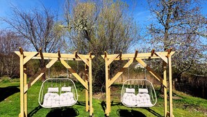Une balançoire en bois avec deux sièges rembourrés, installée dans un espace herbeux.