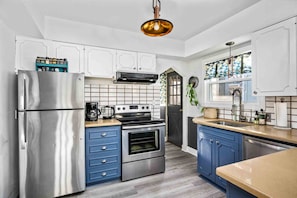 A modern kitchen with stainless steel appliances, blue cabinets, and a geometric backsplash.