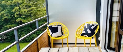 Un balcon avec deux chaises jaunes, une plante en pot et une bougie.