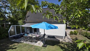 A backyard with a covered patio area, a brick wall, and a house with a dark roof. - Holiday Home in North Holland Near Beach (Sint Maartensvlotbrug)