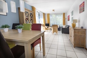A spacious living area with a wooden dining table, chairs, a sofa, and a television. - Holiday Home in North Holland Near Beach (Sint Maartensvlotbrug)